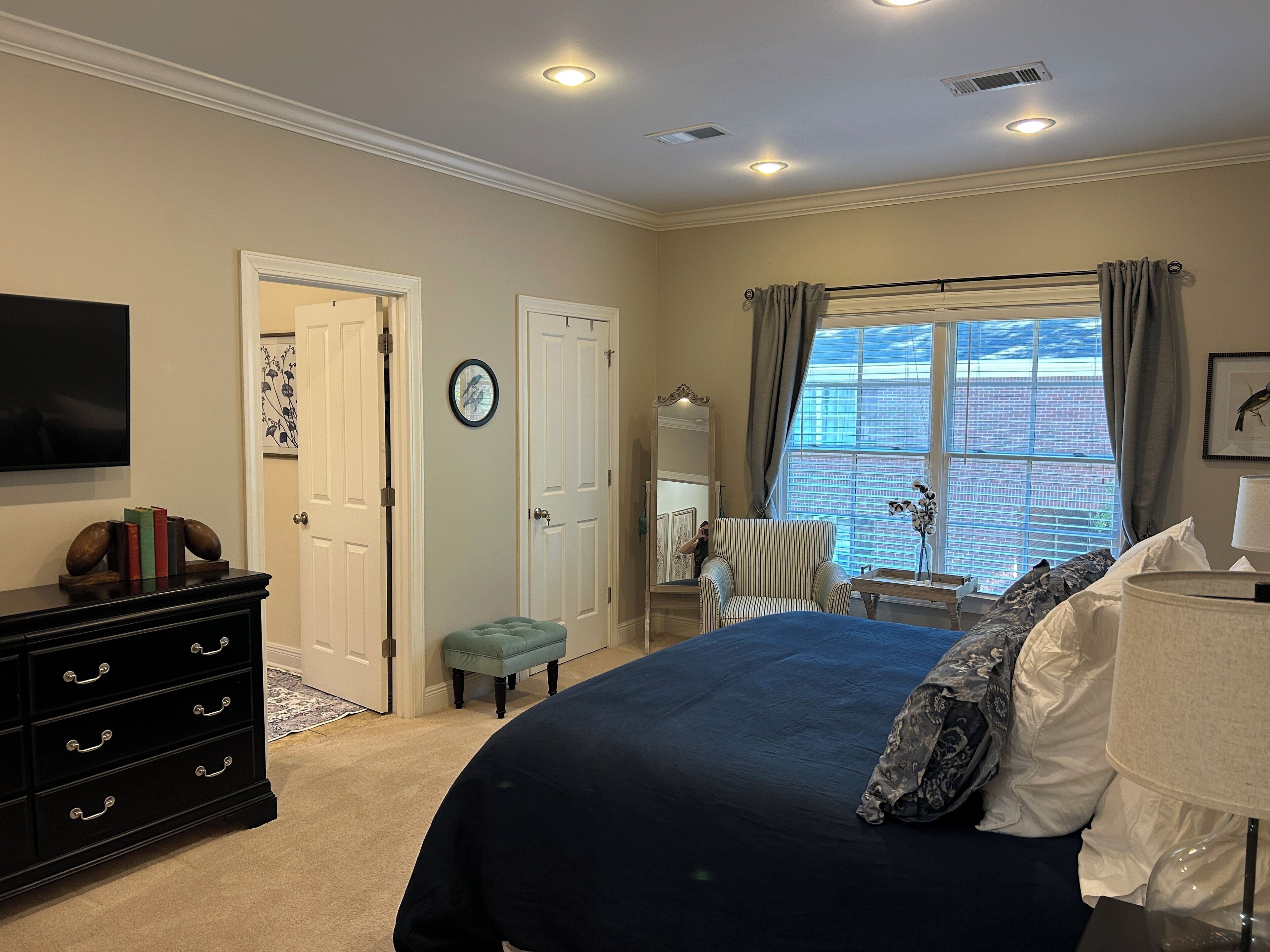 Une chambre à coucher avec un grand lit, une commode, une chaise, un bureau et une fenêtre avec des rideaux.
