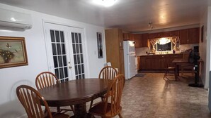A dining area with a round table and four chairs, a kitchen with wooden cabinets, and a window with curtains.