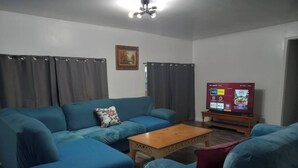 A living room with a blue sofa, a wooden coffee table, and a television displaying various channels.