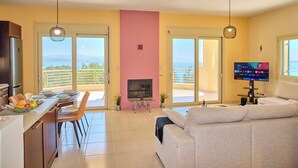 A modern living room with a sofa, a TV, and a dining area with a table and chairs. - Villa Kallisti - Sea View & Private Pool (Corfu)