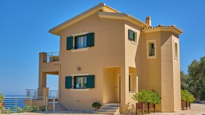 A two-story building with a balcony, a staircase leading to the upper floor, and a small garden area with potted plants. - Villa Kallisti - Sea View & Private Pool (Corfu)