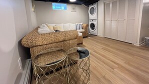 A room with a woven sofa, a small round table, a washing machine, and a closet with louvered doors.