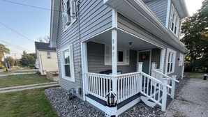A two-story house with a covered porch, a visible number '99', and a gravel driveway.