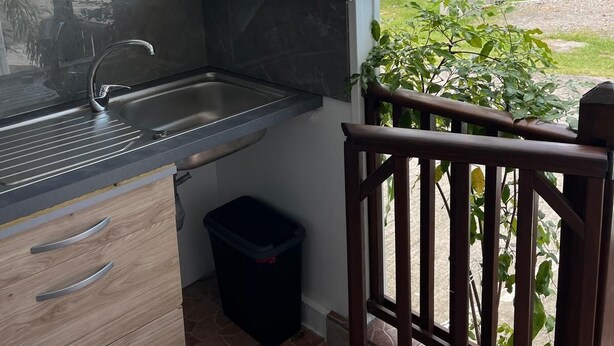 A kitchen with a view of a coastal landscape, a wooden cabinet, a sink, and a trash bin.