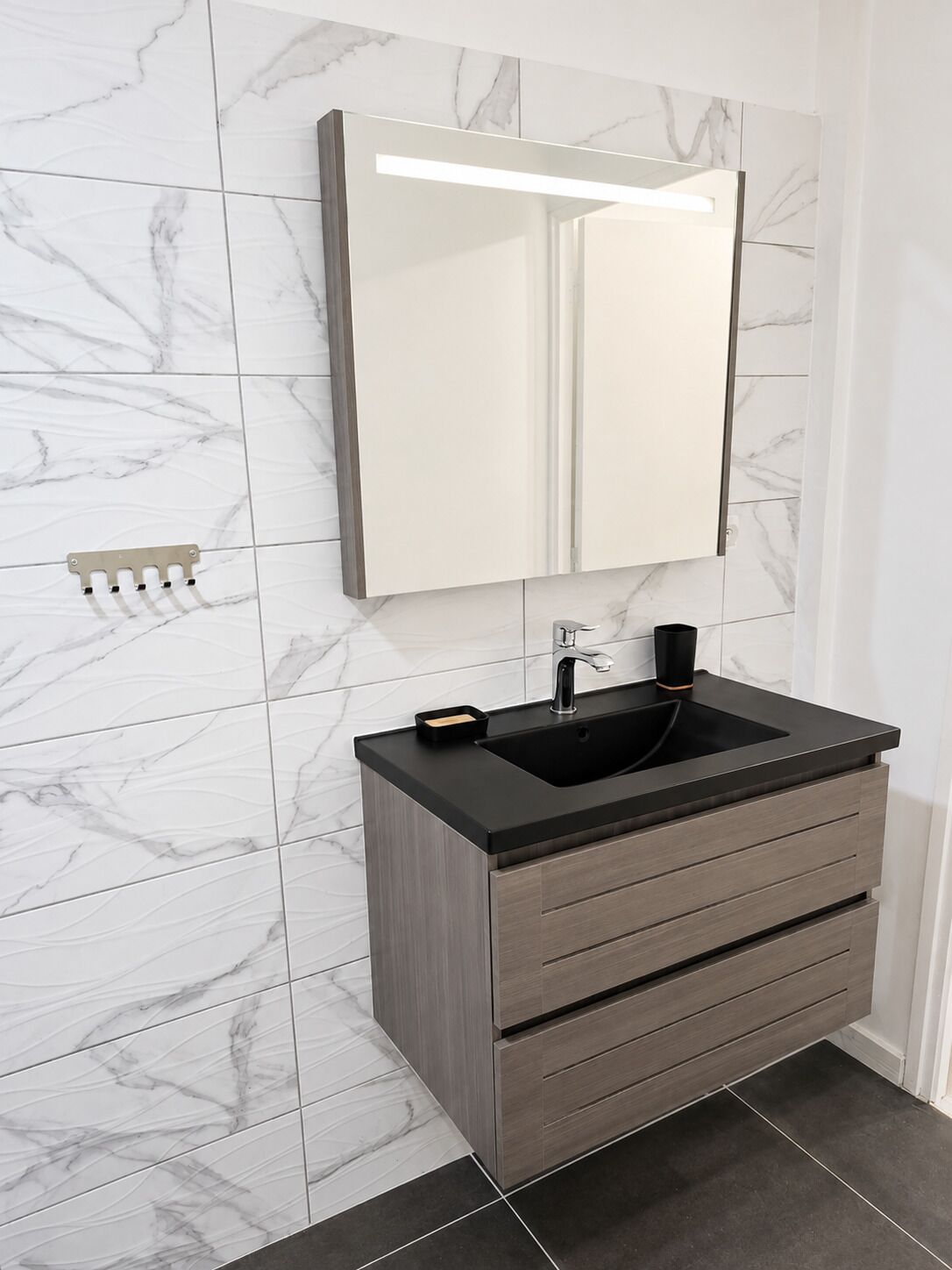 Un bagno con zoccolo in marmo, lavandino nero e mobile vanità in legno con cassetti.