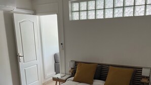 A bedroom with a bed, a ceiling fan, a window with blinds, a bedside table with a lamp, and a door.