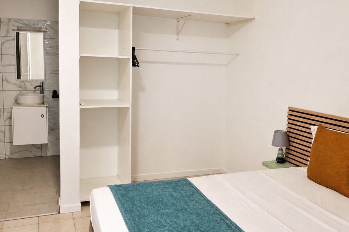 A bedroom with a bed, a nightstand, a lamp, a wooden headboard, and a wardrobe with open doors.