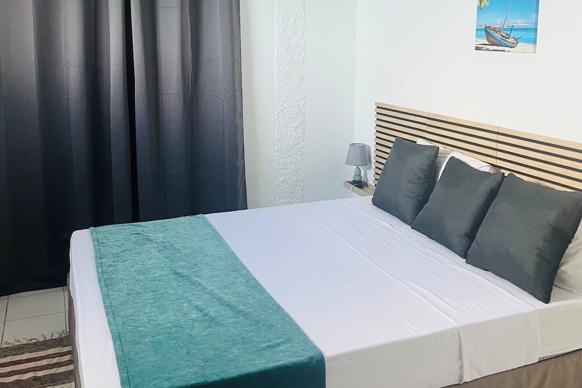A bedroom with a bed, curtains, a painting, and a ceiling fan.