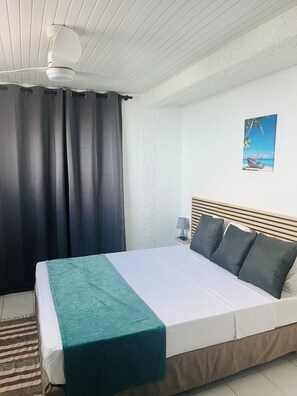 A bedroom with a bed, curtains, a painting, and a ceiling fan. - Résidence hôtelière Le Manguier Panoramique (Trois-Ilets)