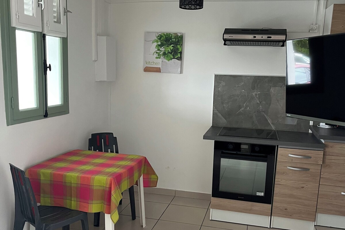 A compact kitchen with a dining area, a television, and a wall-mounted air conditioning unit.