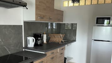A modern kitchen with a black induction cooktop, wooden cabinets, a stainless steel refrigerator, and a black hanging light fixture.