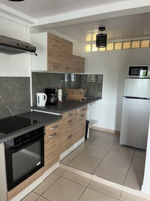 Una cocina moderna con placa de inducción negra, armarios de madera, refrigerador de acero inoxidable y lámpara colgante negra.