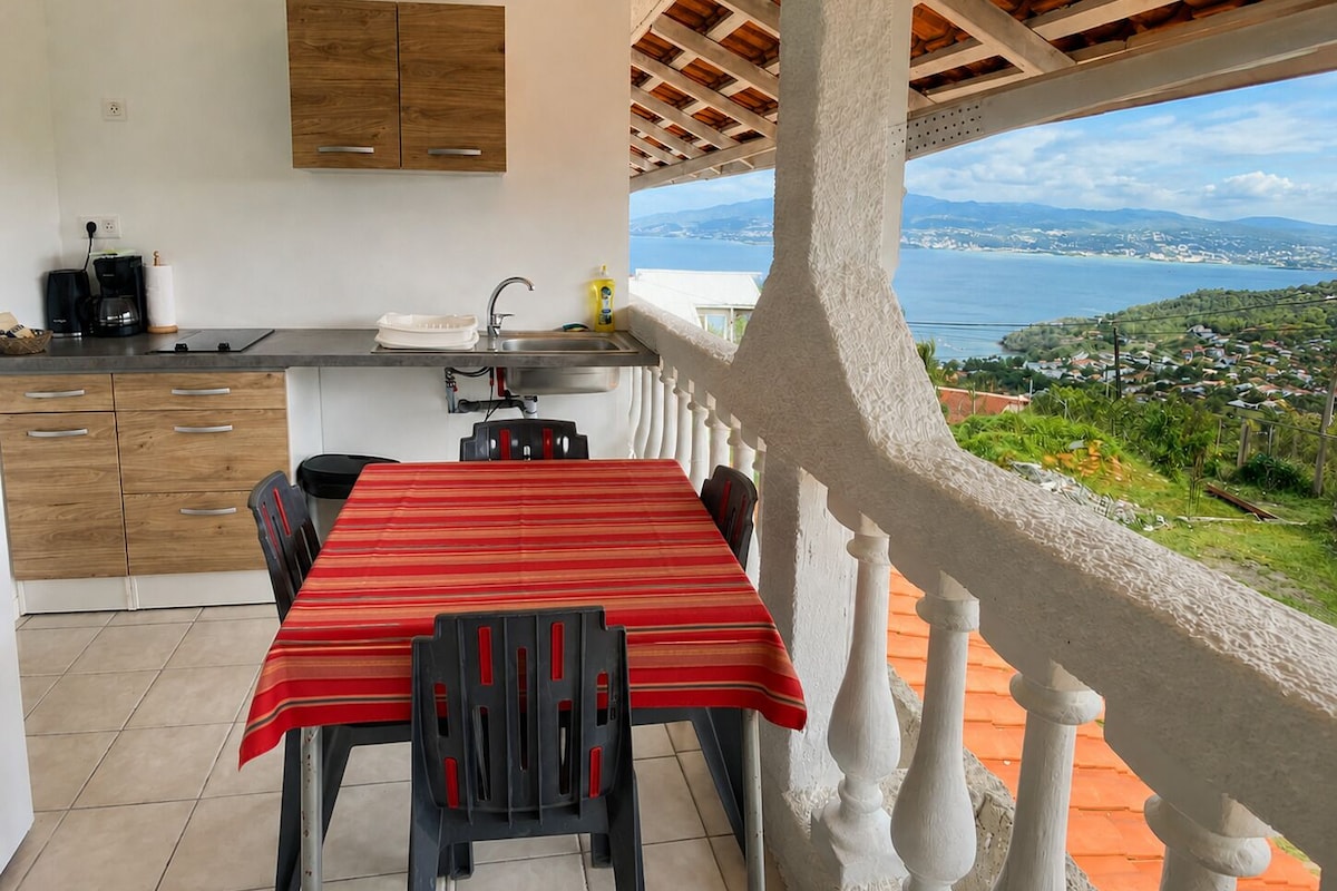 A balcony with a table and chairs, a kitchen area with a sink and cabinets, and a view of a coastal landscape.