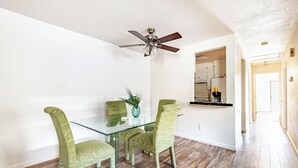 A dining area with a glass table, four patterned chairs, a ceiling fan, and a kitchen visible through an open doorway. - Gated home w/ backyard retreat (Sacramento)