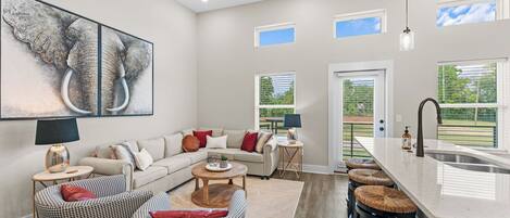 A spacious living area with a sofa, two armchairs, a coffee table, and a kitchen with a large island and bar stools.