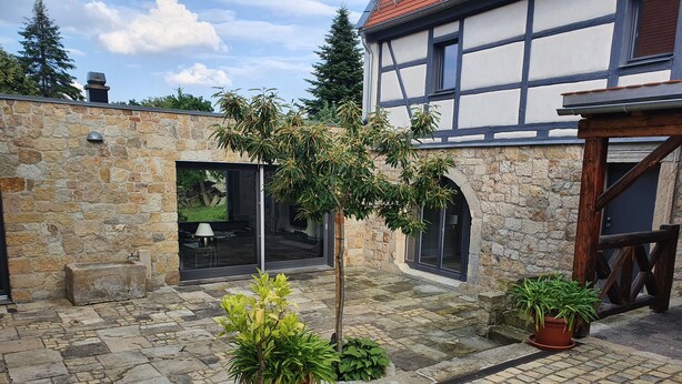 A courtyard with stone walls, potted plants, and a glass door leading to an interior space.