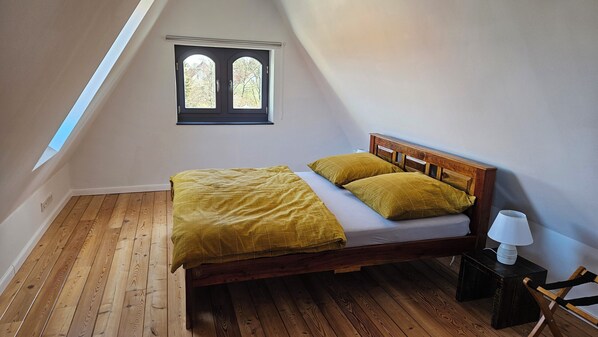 A single bed with a wooden headboard in a room with wooden flooring and a skylight.