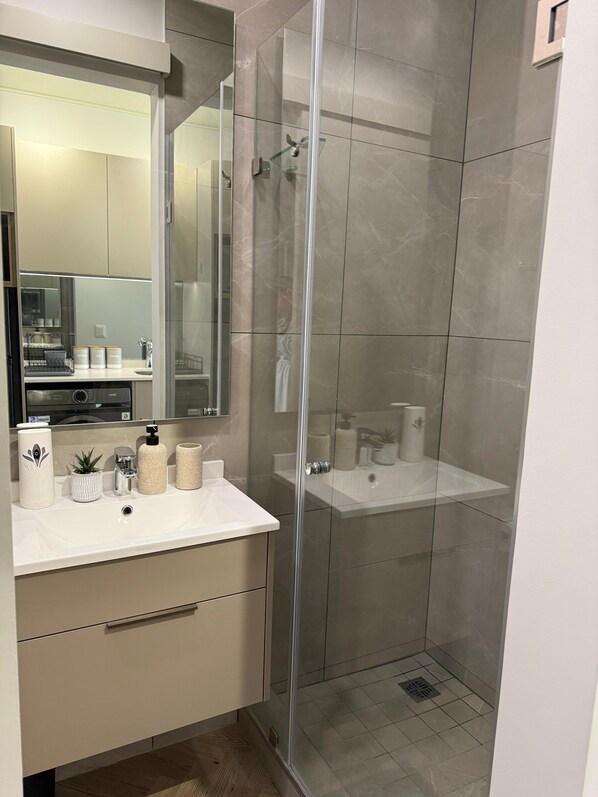 Un baño moderno con ducha de vidrio, tocador con lavamanos y espejo sobre la encimera.