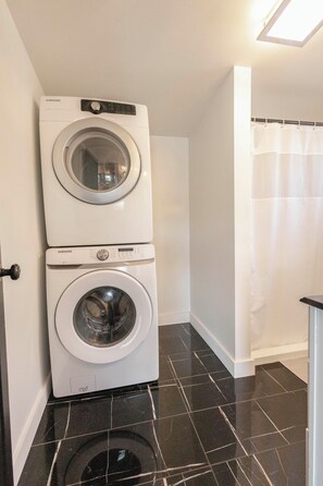 Een wasserette met twee witte Samsung wasmachines, een vloer van zwarte tegels en een witte douchegordijn.