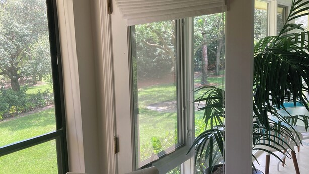 Ein Zimmer mit großen Fenstern, einem weißen Sessel und einem Blumentopf.