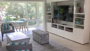 Ein modernes Wohnzimmer mit einem großen Fernseher, weißen Schränken und einem Essbereich mit Tisch und Stühlen.