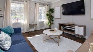 Una sala de estar con un sofá azul, una mesa de centro redonda, un televisor y una planta.