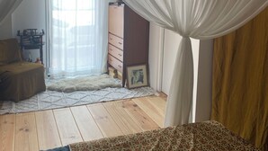 A bedroom with a canopy bed, wooden flooring, a small desk, and a window with sheer curtains. - Comfortable tiny house with kitchen and summer bathroom by the sea (Brem-sur-Mer)