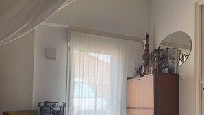 A room with a wooden floor, a brown sofa, a wooden cabinet, and a window with sheer curtains. - Comfortable tiny house with kitchen and summer bathroom by the sea (Brem-sur-Mer)