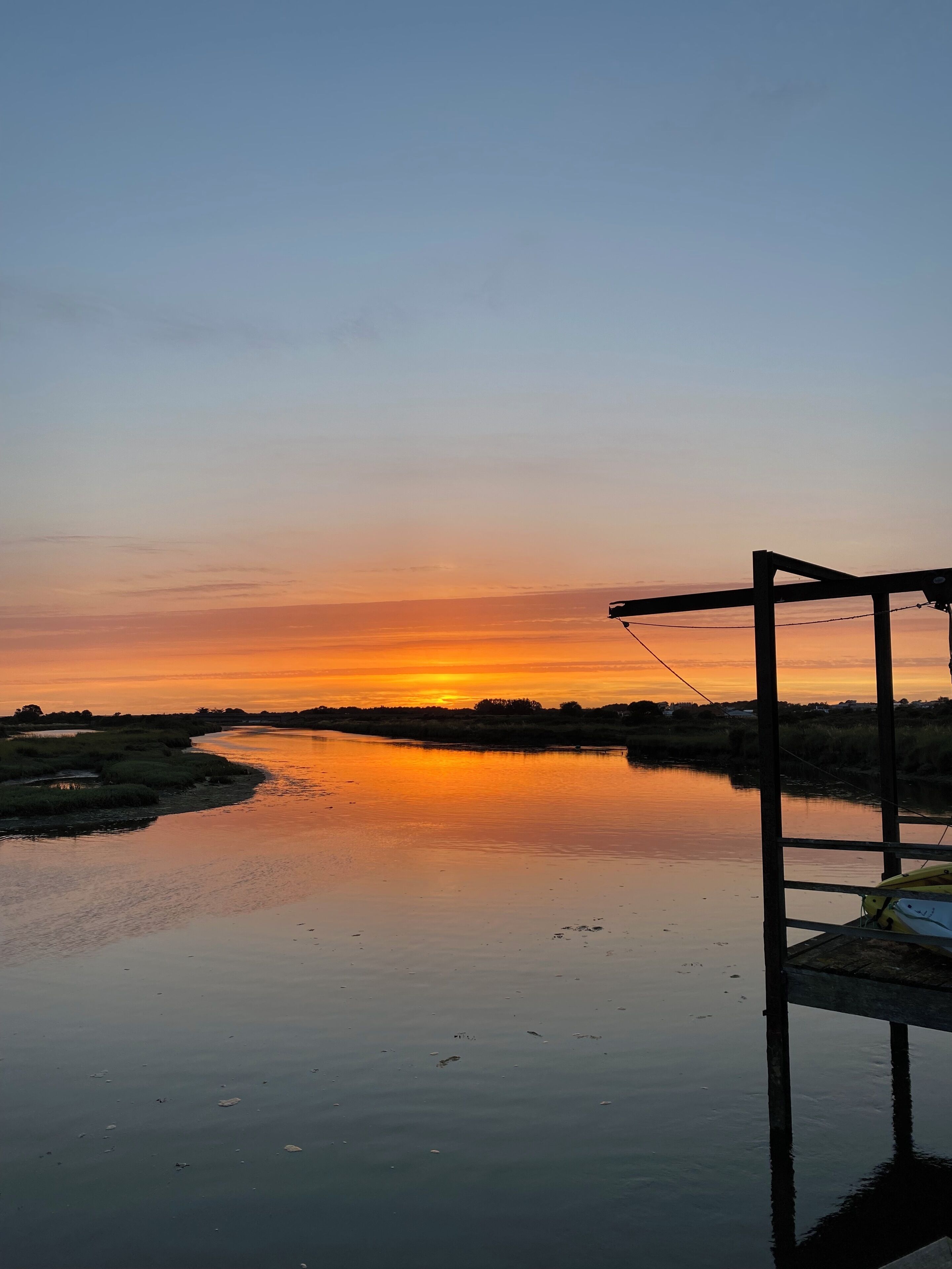 A calm river at sunset with a wooden dock and a kayak.