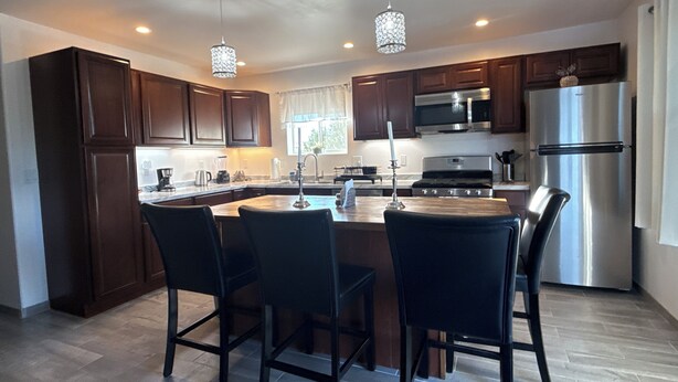 A modern kitchen with dark wooden cabinets, stainless steel appliances, and a central island with bar stools.