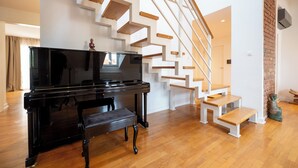 Un salon moderne avec un piano noir, un escalier en bois et une statue.