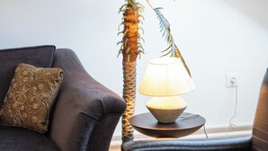 Une pièce avec un canapé de couleur sombre, une petite table avec une lampe et un grand palmier artificiel.