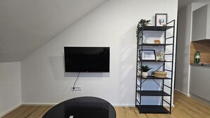 A modern living room with a flat-screen TV mounted on the wall, a black entertainment unit with shelves, and a wooden floor.