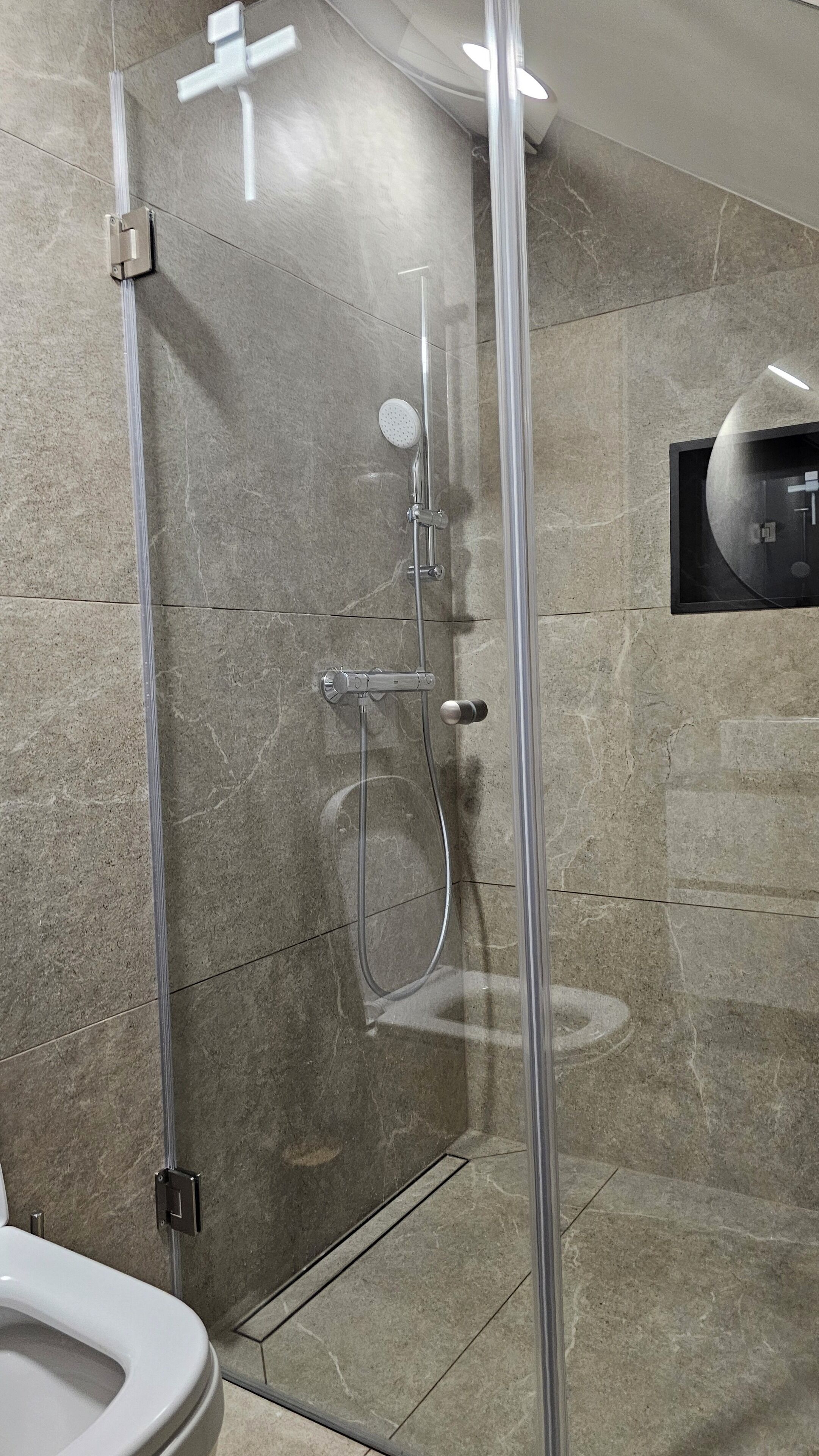 Een moderne badkamer met een douche met glazen wand, een toilet en een bedieningspaneel aan de muur.