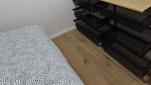 A bedroom with a bed, a wooden desk, a black metal shelving unit, and a wall-mounted coat rack.