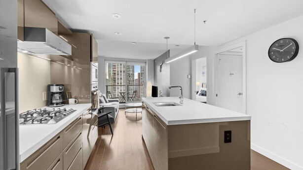 A modern kitchen with a central island, built-in appliances, and a large window overlooking a cityscape. - Elegant 1BR Apt with Pool and Gym, Near Yaletown (Vancouver)