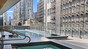 A rooftop pool with a view of high-rise buildings, surrounded by a metal fence. - Elegant 1BR Apt with Pool and Gym, Near Yaletown (Vancouver)