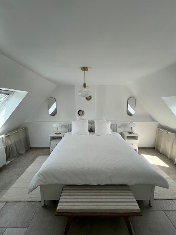 A bedroom with a large bed, a bedside table with a lamp, a bench, and a ceiling light fixture.