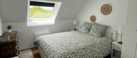 Une chambre à coucher comprenant un lit, une fenêtre, une table de chevet, une lampe, une commode, une chaise et un tapis.