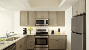 A modern kitchen with stainless steel appliances, a granite countertop, and neutral-toned cabinetry. - Ocean Enclave, a Hilton Grand Vacations Club. (Myrtle Beach)