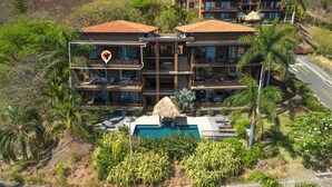 A multi-story hotel with a swimming pool, surrounded by tropical vegetation.