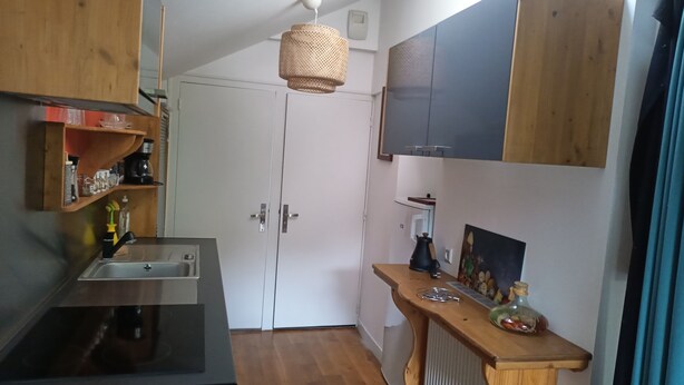 Une cuisine compacte dotée d’une cuisinière intégrée, d’un évier, de meubles en bois et d’un luminaire suspendu.