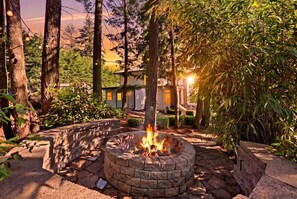 A stone fire pit surrounded by a stone patio, with a house and trees in the background. - Mt Scott Forest Estate— Theater, Sauna, Game Room, Firepit, 15 Min PDX, Sleeps 9 (Happy Valley)