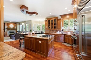 Een ruime keuken met een groot eiland, houten keukenkastjes en moderne apparatuur.