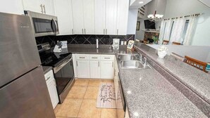 A modern kitchen with white cabinets, a stainless steel refrigerator, a microwave, and a granite countertop.