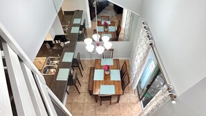 A dining area with a chandelier, a kitchen in the background, and a stone fireplace.