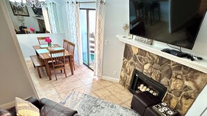 A living room with a leather sofa, a flat-screen TV, a stone fireplace, and a dining area with a table and chairs.