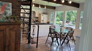 Una cocina amplia con escaleras de madera, ventanas grandes y un comedor con sillas de mimbre.