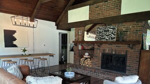 Una sala acogedora con chimenea de ladrillo, techo de madera y un comedor con taburetes.