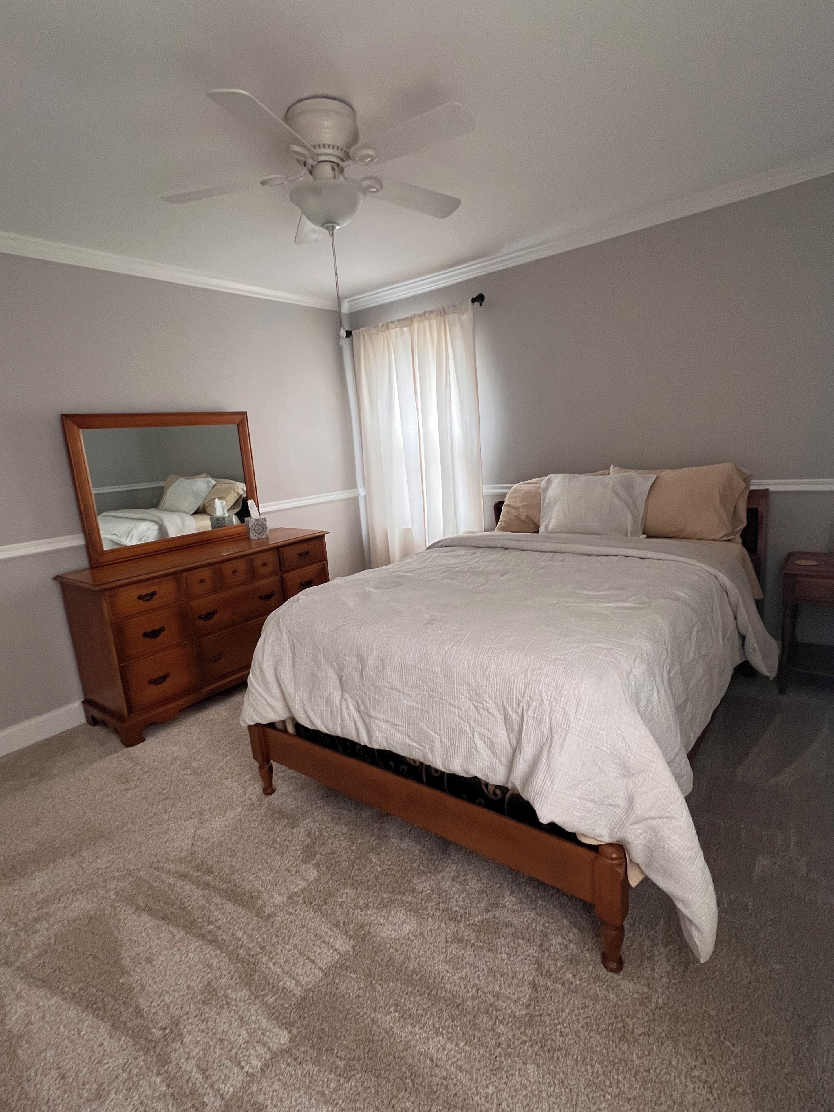 Een slaapkamer met een bed, een dressoir, een spiegel en een plafondventilator.